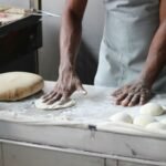 A baker in an indoor kitchen kneading dough for bread preparation, showcasing traditional baking techniques.