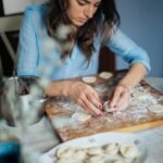 A woman carefully prepares homemade pastries on a wooden board in a cozy kitchen setting.