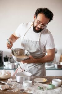 A male chef in an apron mixes batter in a modern kitchen setting, focusing on technique.